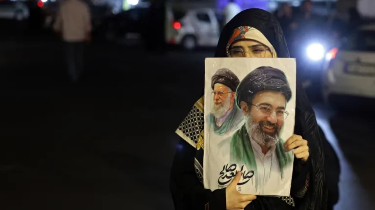 Seorang perempuan memegang plakat bergambar Pemimpin Tertinggi Iran Ayatollah Mojtaba Khamenei dan pendahulu sekaligus ayahnya yang telah wafat, Ayatollah Ali Khamenei, dalam aksi protes anti-Amerika Serikat dan Israel di Lapangan Hafte Tir, Teheran, pada 17 Mei 2026. (AFP)