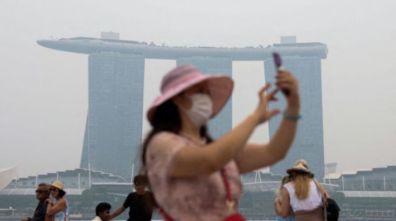 Seorang wisatawan yang mengenakan masker tampak memotret saat kabut asap menyelimuti Merlion Park di Marina Bay, dengan resor Marina Bay Sands sebagai latar belakangnya, di Singapura pada Jumat, 16 Oktober 2026. (IDNVoice/Reuters)